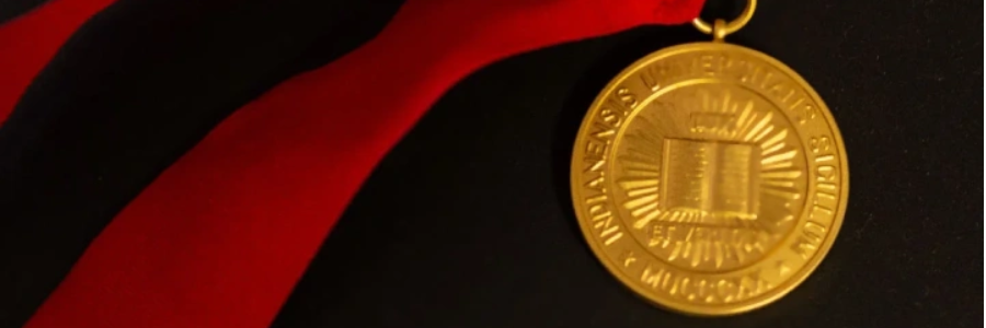 A gold IU medal strung on red ribbon sits on a black velvet background.